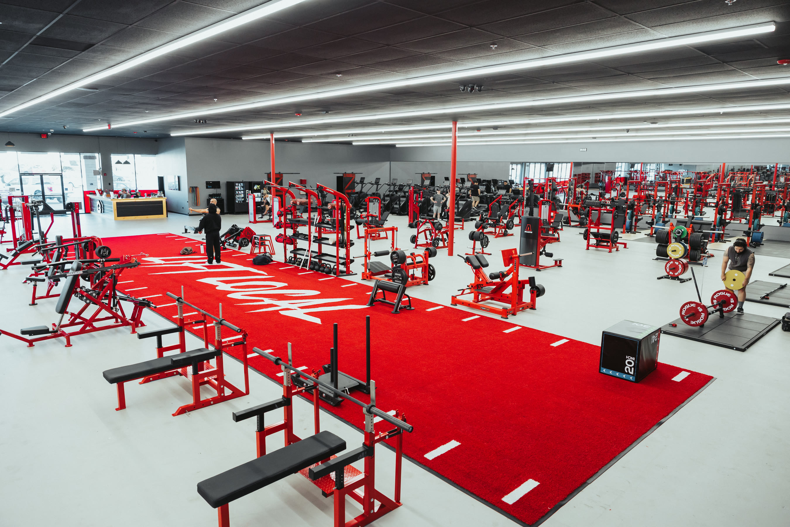 The Camarillo floor — red turf runway with the House of Gains logo, custom red machines and racks down both sides